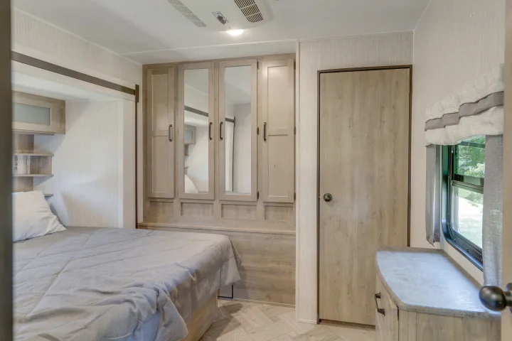 Bright, modern RV rental bedroom featuring a comfy bed, mirrored cabinets, AC, and a window for scenic views.. Palomino Puma Park Trailer for Temporary Housing 2021