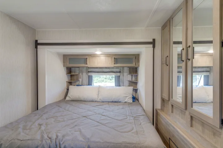 Compact RV rental bedroom with a comfy bed, integrated storage, window, and mirrored closet. Ready for adventure.. Palomino Puma Park Trailer for Temporary Housing 2021