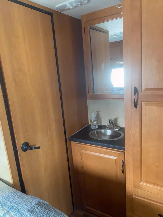 Compact RV rental bathroom/bedroom area with sink, mirrored cabinet, door, and wooden storage.. Thor Motor Coach Four Winds Majestic 2013