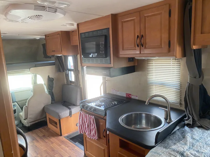 Explore this functional RV rental interior: kitchen with microwave & stove, dinette, overhead bunk, and cockpit access.. Thor Motor Coach Four Winds Majestic 2013