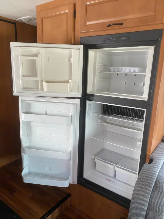Empty and open RV refrigerator with upper freezer and lower fridge, featuring shelves & door bins, great for an rv rental.. Thor Motor Coach Four Winds Majestic 2013