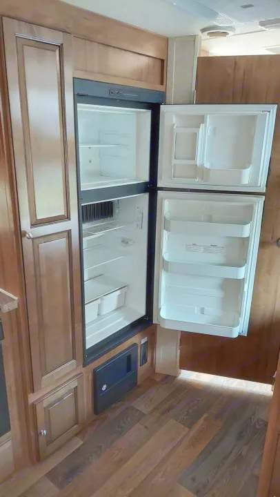 Open RV refrigerator, empty and ready for use in this rv rental, with wood cabinetry and paneling completing the interior.. Other Other 2016