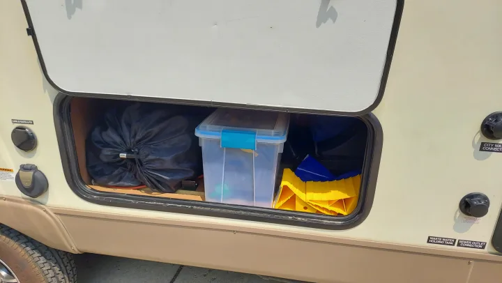 RV rental exterior compartment reveals organized camping gear: a black bag, clear bin, yellow leveling blocks, and utility hookups.. Other Other 2016