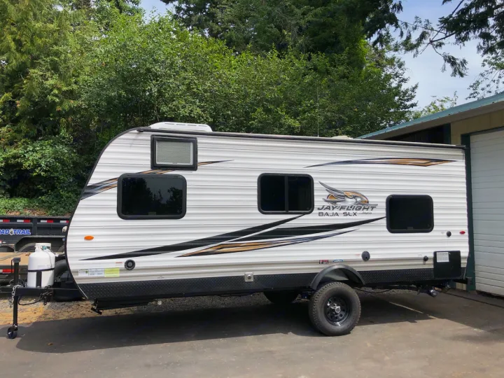 White Jayco Jay Flight Baja SLX travel trailer for rv rental. This rugged camper, with off-road tires, is parked outdoors.. Jayco Jay Flight 2019