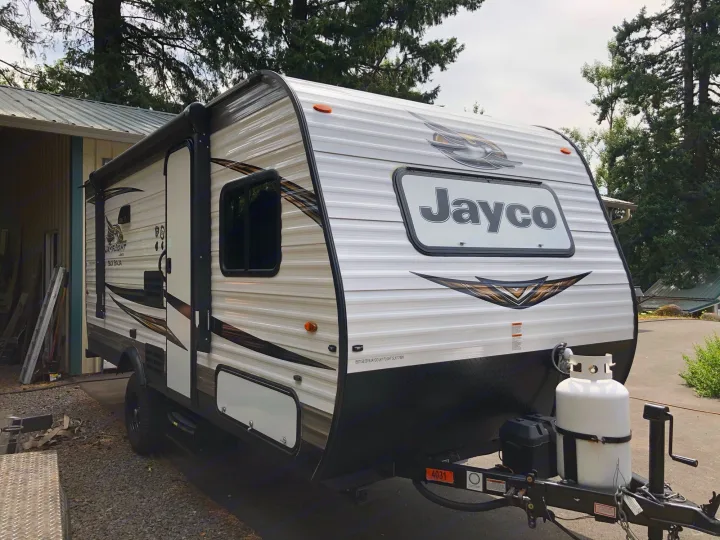 This white Jayco Jay Flight SLX travel trailer, perfect for an rv rental, is parked outdoors with a propane tank.. Jayco Jay Flight 2019