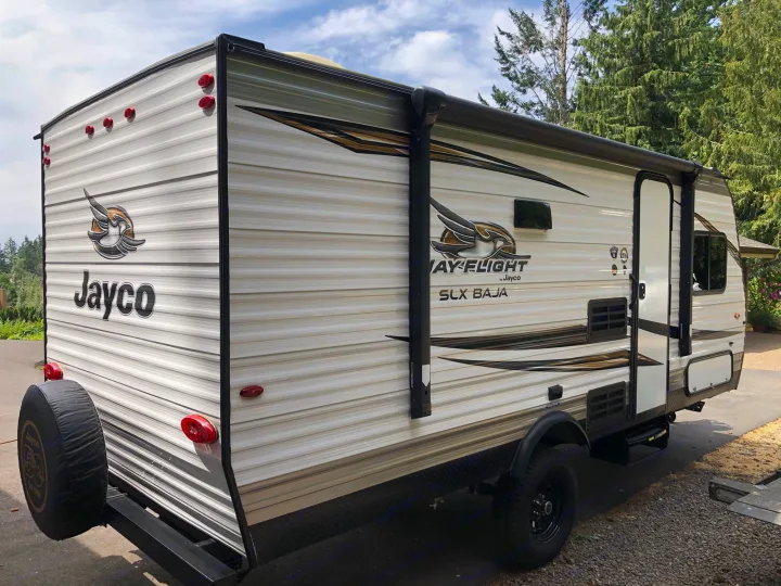 Side and rear view of a Jayco travel trailer, an excellent RV rental option, parked outdoors with a retracted awning.. Jayco Jay Flight 2019