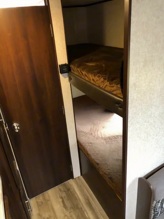 Inside an **rv rental**: dark wood door opens to cozy bunk beds with blankets. A Dometic control is on the wall.. Jayco Jay Flight 2019