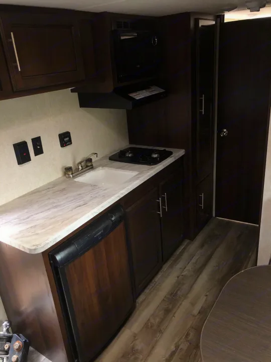 RV rental kitchen: light countertop with sink, stove, overhead microwave, and integrated fridge. Dark wood cabinets and flooring.. Jayco Jay Flight 2019
