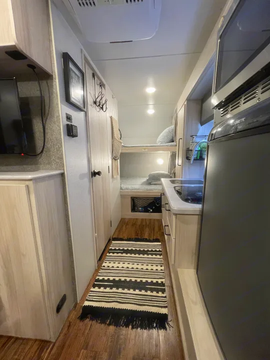 Inside an rv rental: a cozy hallway with bunk beds, a compact kitchen, and a patterned rug on wood flooring.. Winnebago Hike 2021