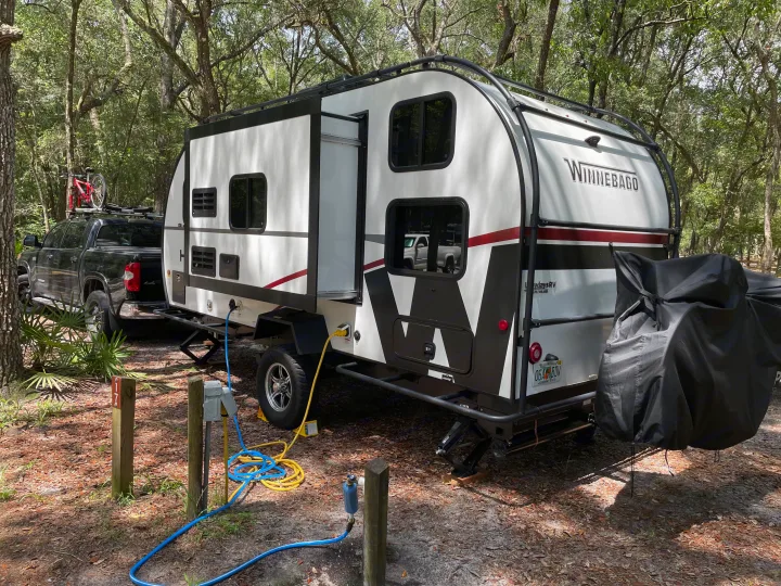 A Winnebago rv rental is parked at a shaded campsite (site 17), hooked up to utilities, with a truck and bike.. Winnebago Hike 2021