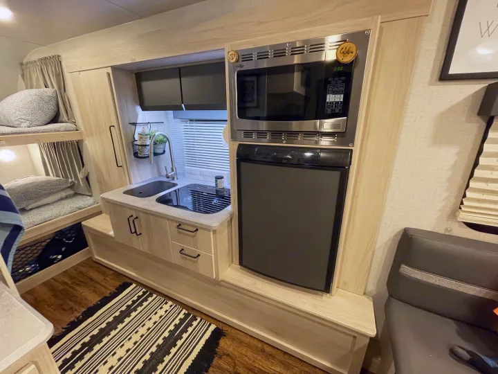 Compact RV rental interior featuring a kitchen with sink, stovetop, microwave, fridge, and cozy bunk beds.. Winnebago Hike 2021