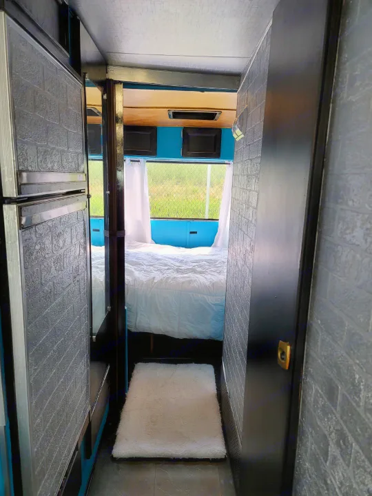 Cozy RV rental: Dark hallway leads to a bedroom with white bedding & a bright window view of green fields.. Chevrolet Other 1980
