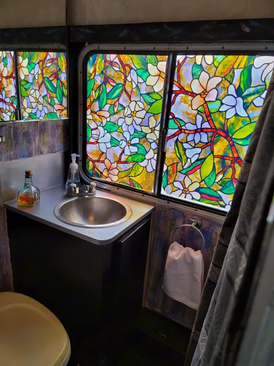 Unique RV rental bathroom featuring a vibrant floral stained-glass window, sink, and toilet. Enjoy colorful travels!. Chevrolet Other 1980