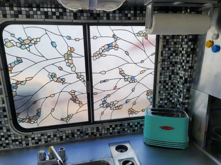 Cozy RV rental kitchen featuring a unique, branch-patterned window, retro blue toaster, and black-and-white tile backsplash.. Chevrolet Other 1980