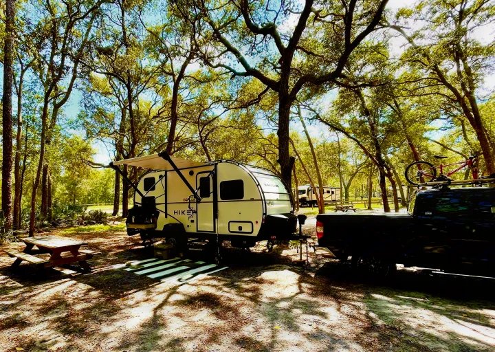 RV rental campsite: Winnebago Hike teardrop trailer hitched to truck with bike, sunny trees, picnic area.. Winnebago Hike 2021