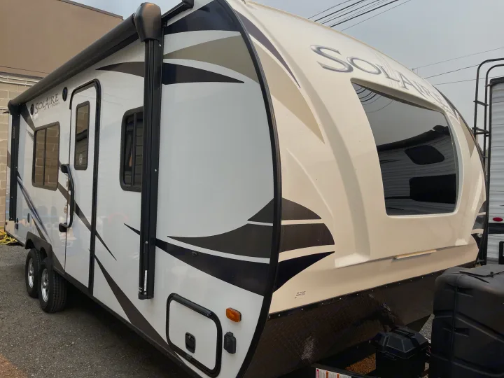 A bright white Solaire travel trailer with black and tan graphics, ready for an RV rental adventure.. Solaire 211BH 2019