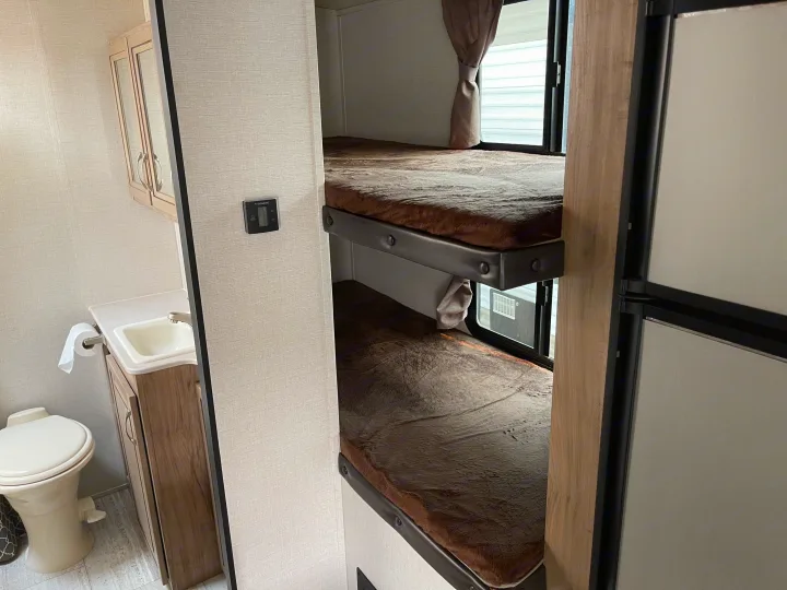 Cozy RV rental interior featuring a compact bathroom with toilet and sink, alongside built-in bunk beds. Includes Dometic control.. Solaire 211BH 2019