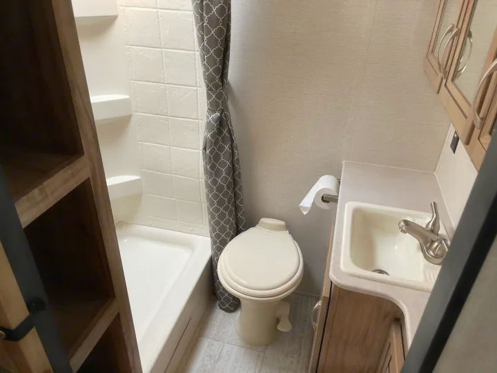 Compact RV rental bathroom showcasing a shower, toilet, sink, and convenient built-in shelving.. Solaire 211BH 2019