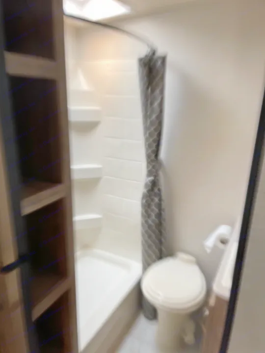 Compact RV rental bathroom: Features a white shower with shelves, a grey shower curtain, and a white toilet.. Solaire 211BH 2019