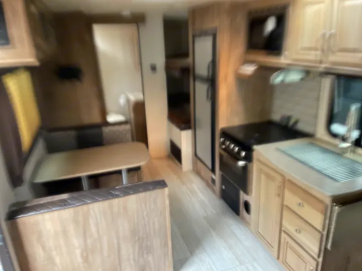 Interior of a modern RV rental, showcasing a kitchen with stove, sink, fridge, and a cozy dining booth.. Solaire 211BH 2019