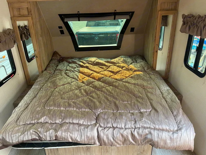 This RV rental showcases its comfortable bedroom with a patterned comforter, front window, and mirrored cabinet.. Solaire 211BH 2019
