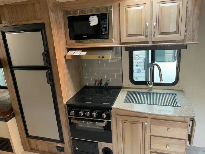 Modern RV rental kitchen interior: fridge, microwave, oven/stove, sink, and wood cabinets.. Solaire 211BH 2019