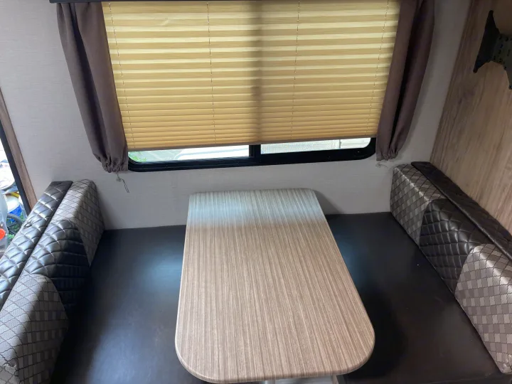 Spacious RV rental dinette with a light wood table, dark quilted bench seats, and window blinds. Perfect for meals on the go.. Solaire 211BH 2019