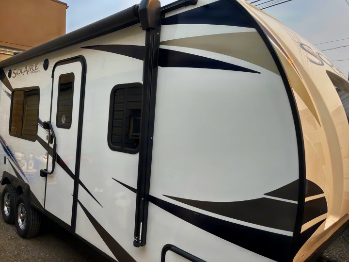 Modern white travel trailer RV rental with a black extendable awning and bold side graphics, ready for your adventure.. Solaire 211BH 2019