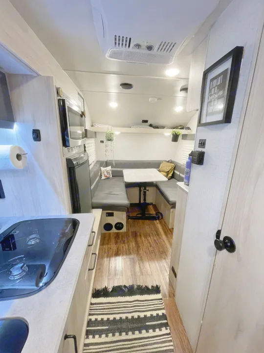 Inside an RV rental: a compact kitchen, dinette, comfortable seating, and overhead storage, all with wood-look flooring.. Winnebago Hike 2021
