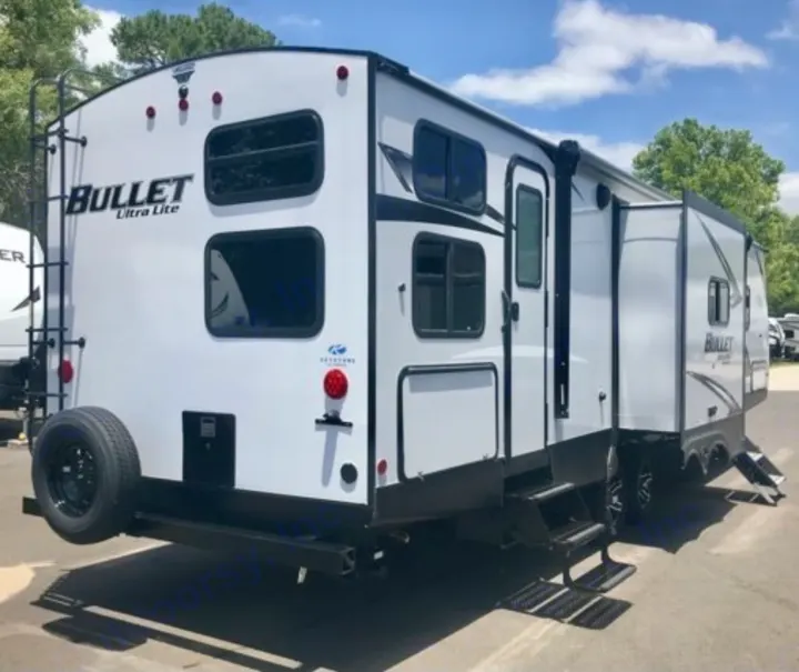 White Bullet Ultra Lite travel trailer RV rental, parked outdoors. Features a ladder, spare tire, and sleek design.. Keystone Bullet 2021