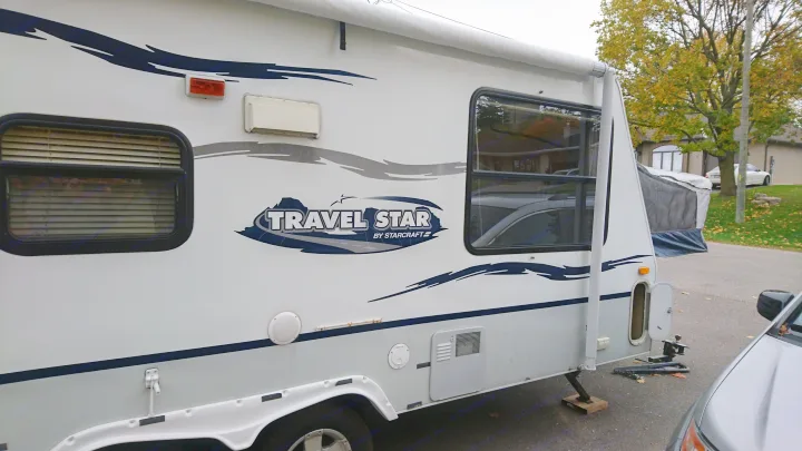Exterior side view of a white Travel Star RV rental, featuring windows, an awning, and graphics, parked outdoors.. Starcraft Travel Star 2007