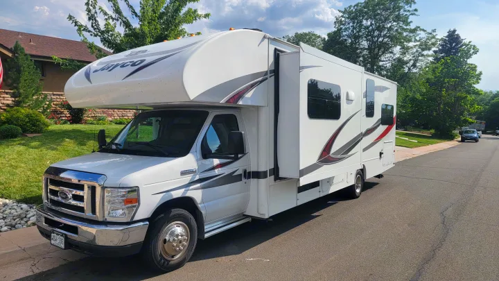 This white Jayco Class C **RV rental** with an extended slide-out is parked on a residential street, ready for adventure.. Jayco Redhawk 2018
