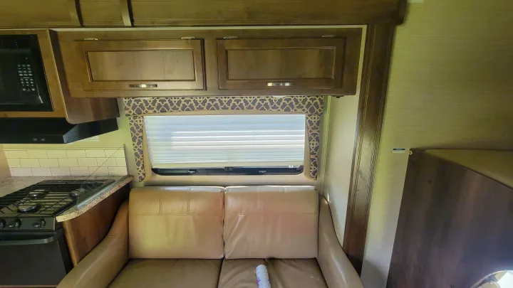 RV rental interior featuring a compact kitchen (stove, microwave), overhead cabinets, comfortable sofa, and a window.. Jayco Redhawk 2018