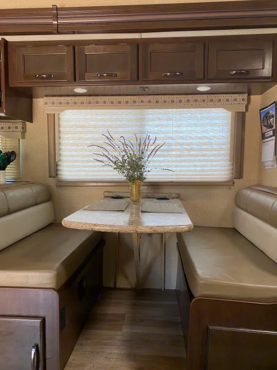 RV rental interior featuring a cozy dinette, dark wood cabinets, and a bright window with blinds.. Thor Four Winds 2020