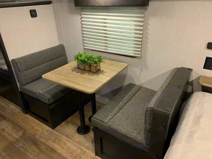 Cozy RV rental dinette with grey upholstered benches, a light wood table, and plant, perfect for meals & relaxation.. Forest River Cherokee Wolf Pup 2022