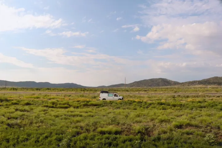 A white camper van, resembling an RV rental, is centered in a wide, verdant field with distant hills under a partly cloudy sky.. Ford Ford E350 2011
