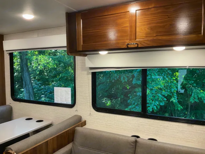 Inside an RV rental: cozy dinette, overhead cabinets, and large windows offering vibrant green nature views. Relax and enjoy.. Winnebago Outlook 2020
