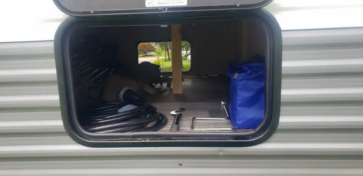 Inside an RV rental's pass-through storage: a power cord, camping tools, and blue bag are neatly stored.. KZ Sportsmen 180BH 2021