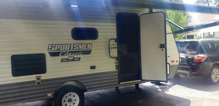 SPORTSMEN Classic travel trailer with open door and extended awning, perfect for an RV rental adventure.. KZ Sportsmen 180BH 2021