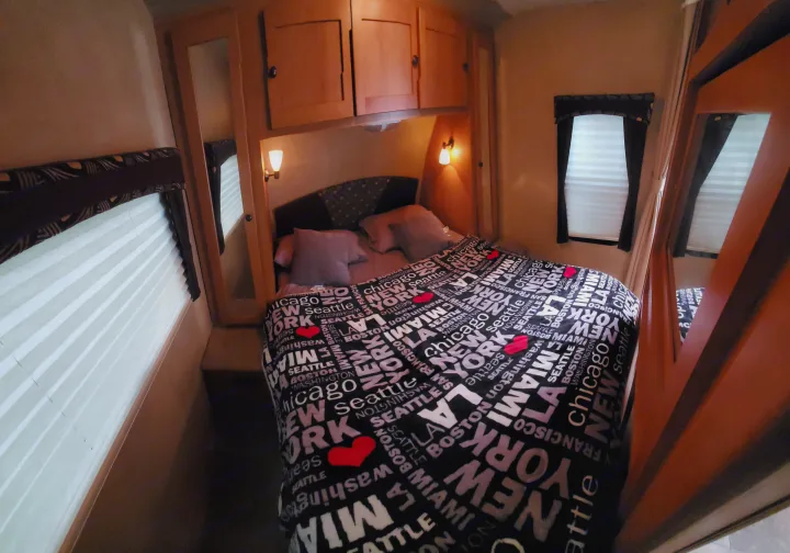 Cozy RV rental bedroom featuring a bed with city-themed comforter, overhead storage, lights, and windows.. Cruiser Rv Corp Shadow Cruiser 2012