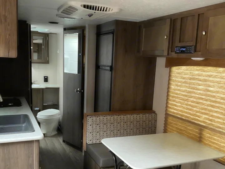 Spacious RV rental interior featuring a compact kitchen, bathroom, refrigerator, and comfortable dinette area.. Coachmen Clipper 2019