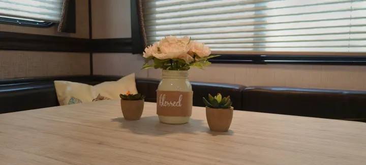 Cozy RV rental dinette featuring a light wood table with flowers and succulents, beside dark booth seating.. Heartland Pioneer 2021