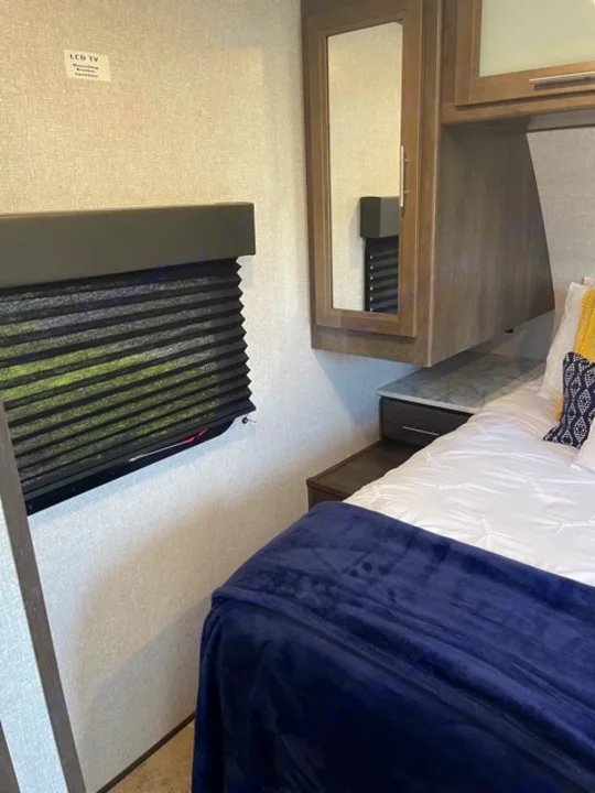 Step into comfort: This RV rental bedroom features a cozy bed, built-in storage with a mirror, and window blinds for privacy.. Dutchmen Coleman 2021