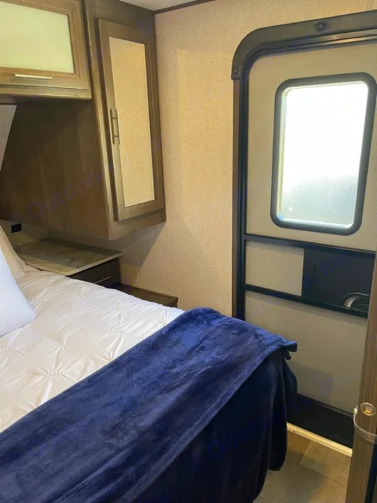 Inside an RV rental bedroom featuring a bed, overhead cabinets, and bright window.. Dutchmen Coleman 2021