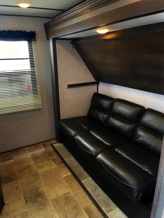 Spacious RV rental living area featuring a black leather sectional sofa, sleek wood trim, and a mix of carpet/tile flooring.. Dutchmen Coleman 2021