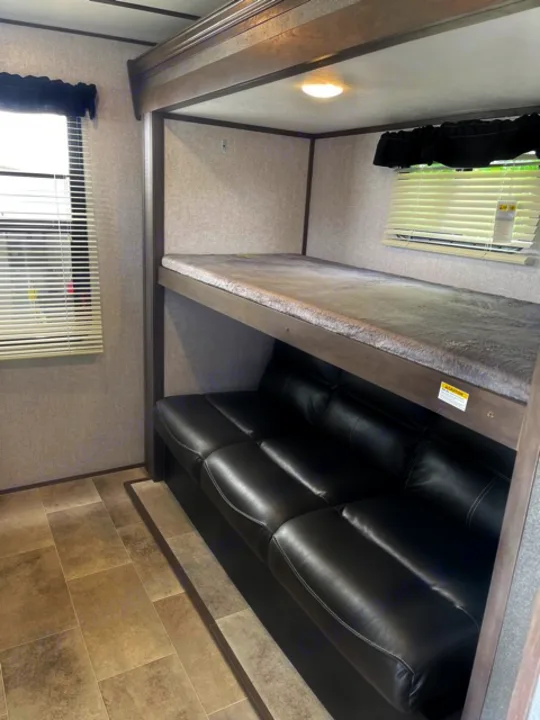 RV rental interior: Comfortable dark leather sofa below a carpeted bunk bed, modern walls with trim, and tiled floor.. Dutchmen Coleman 2021