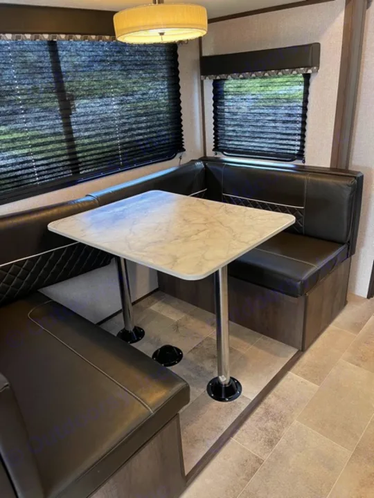 RV rental interior: A practical dinette with black leatherette benches, a faux marble table, and dark pleated window blinds.. Dutchmen Coleman 2021
