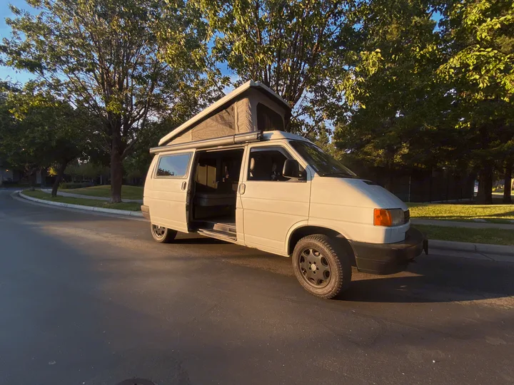 White VW Eurovan pop-top camper van parked on a sunny street, door open revealing interior, perfect for RV rental.. Volkswagen T4 Multivan Westfalia 1995