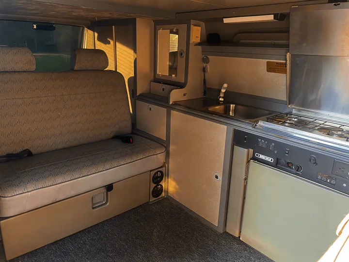 Compact RV rental interior featuring a versatile bench seat, kitchenette with sink & stove, plus integrated storage for your adventures.. Volkswagen T4 Multivan Westfalia 1995