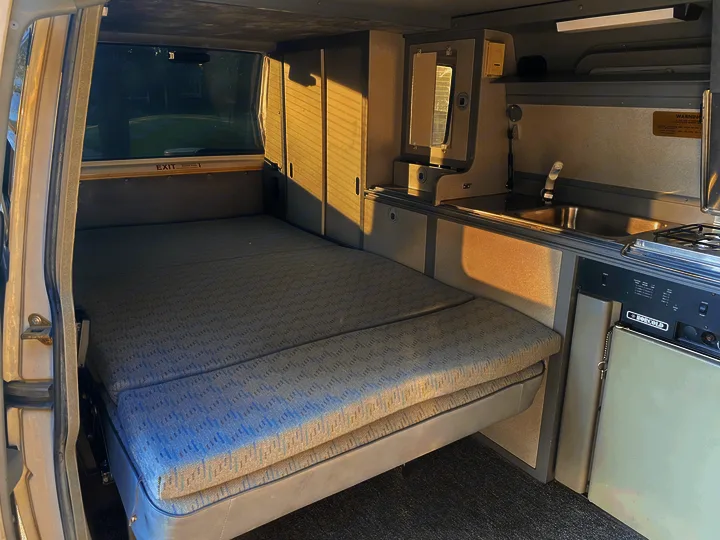 RV rental interior: a comfy bed, compact kitchen with sink/stove, and cabinet storage for road trips.. Volkswagen T4 Multivan Westfalia 1995